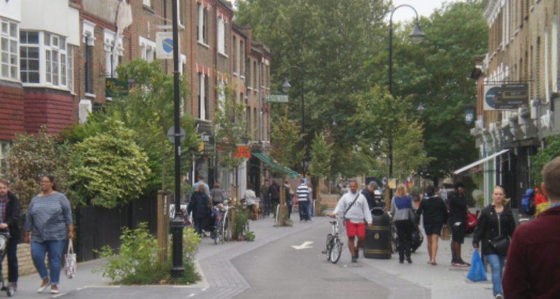 A low traffic neighbourhood with shops, planters, pedestrians and a traffic free road